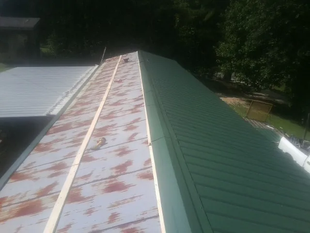 Old rusted panels beside newly installed green metal roofing — Wind Damage Roof Repair by Roofing Brothers in Verbank