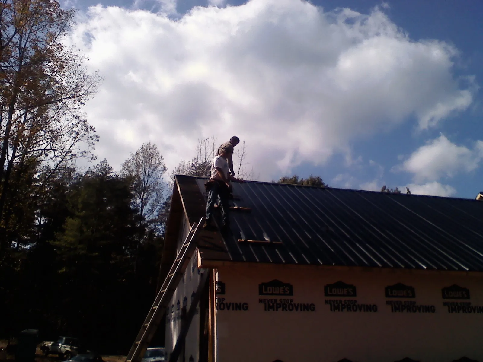 Roofer fastening dark metal panels high against a cloudy sky, from a Roof Inspection job in Verbank