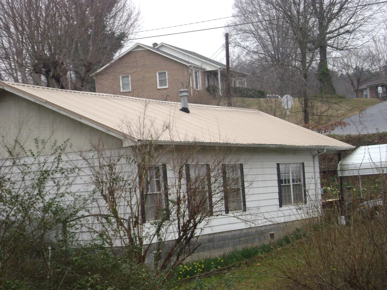 Tan metal roof on a white sided house set into a hillside — Commercial Roofing by Roofing Brothers in Verbank